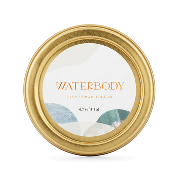 A golden tin of Fisherman's Balm sits agains a white backdrop. The tin features a white round label with blue and green imagery and gold foil text